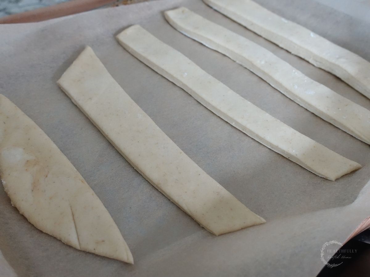 sourdough breadstick dough in strips on a parchment lined baking sheet rpior to proofing so you can see how flat they are