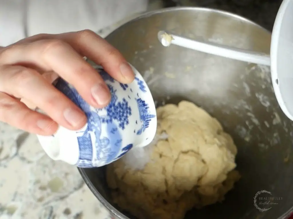 adding salt from a blue and white china jar to sourdough breadstick dough in a kitchenaid stand mixer
