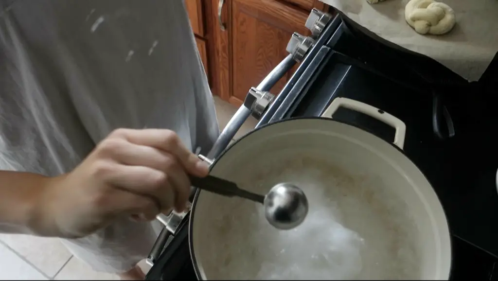adding baking soda using a measuring spoon to a white dutch oven filled with boiling water 