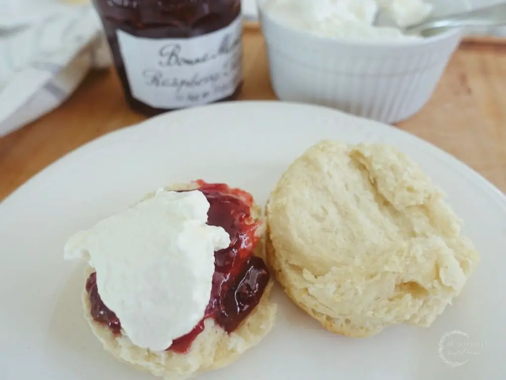 lemonade scones topped with jam and cream on a white plate with the top of the scone resting on the bottom