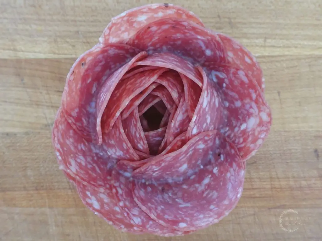 salami rose sitting on a wooden cutting board to display how to make a salami rose