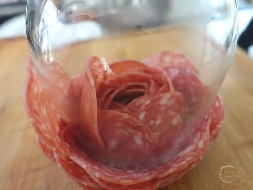 salami rose inside of a glass on top of a wooden cutting board