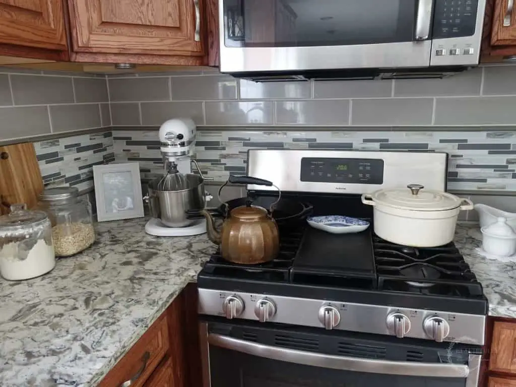 glass jars with flour and oats inside, a wooden cutting board, a white kitchenaid stand mixer, copper tea kettle, white dutch oven, all in a kitchen listing off kitchen essentials for a new home