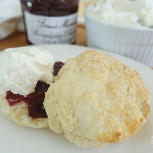 lemonade scones no cream with homemade whipped cream and jam on a white plate with the jam and cream jar in background