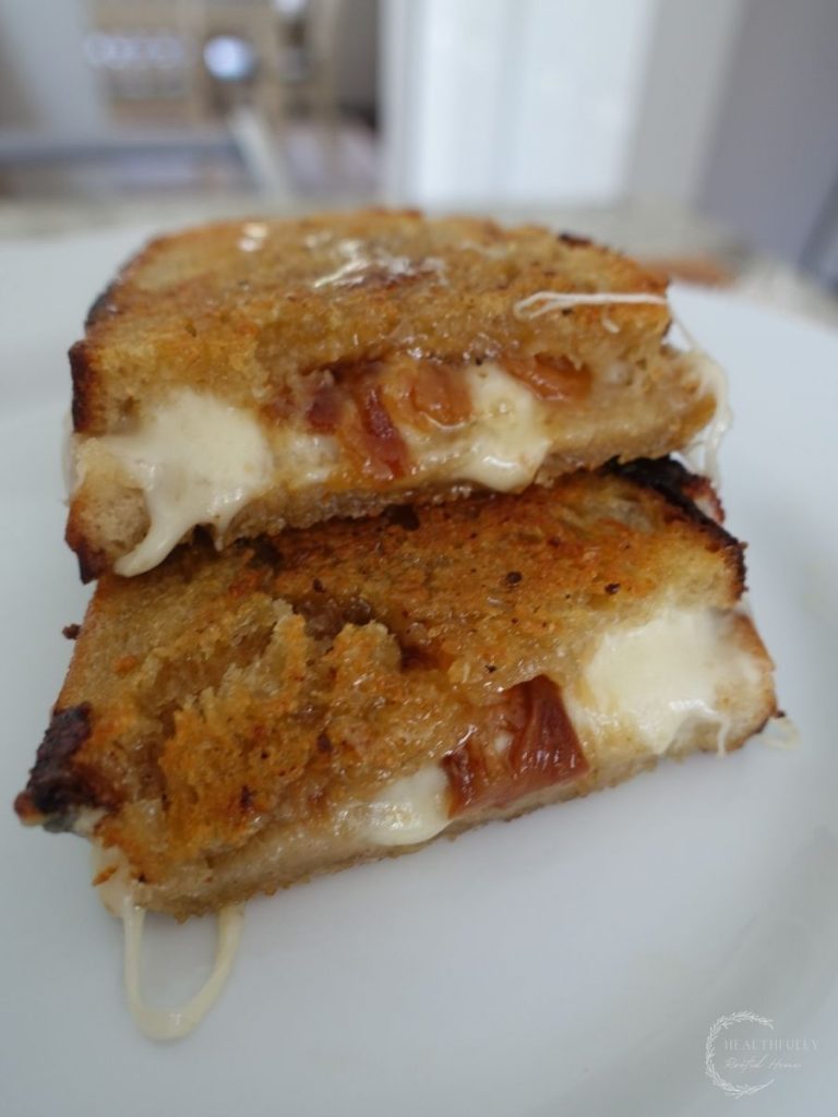 provolone grilled cheese sandwiches halved and stacked on a white plate with garlic confit and provolone cheese on the inside and honey on top the crusty bread