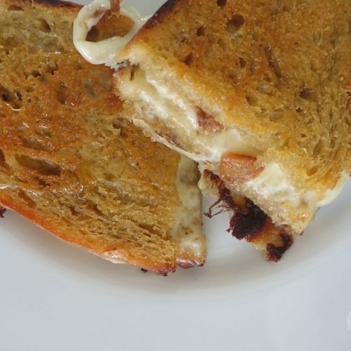 provolone grilled cheese sandwich with honey and garlic confit spread on homemade sourdough bread on a white plate with melted cheese dripping out