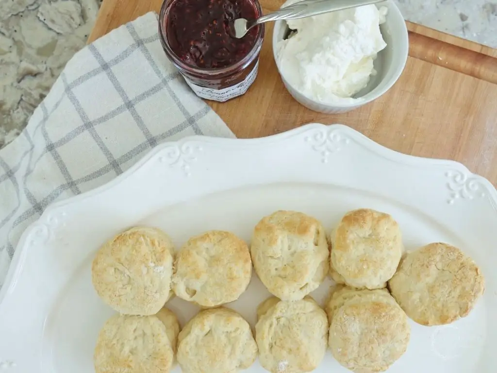 baked lemonade scones next to whipped cream and jam on a white serving platter