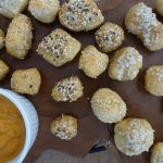 sourdough pretzel bites baked to golden brown topped with seasonings and placed on a wooden block next to cheese sauce