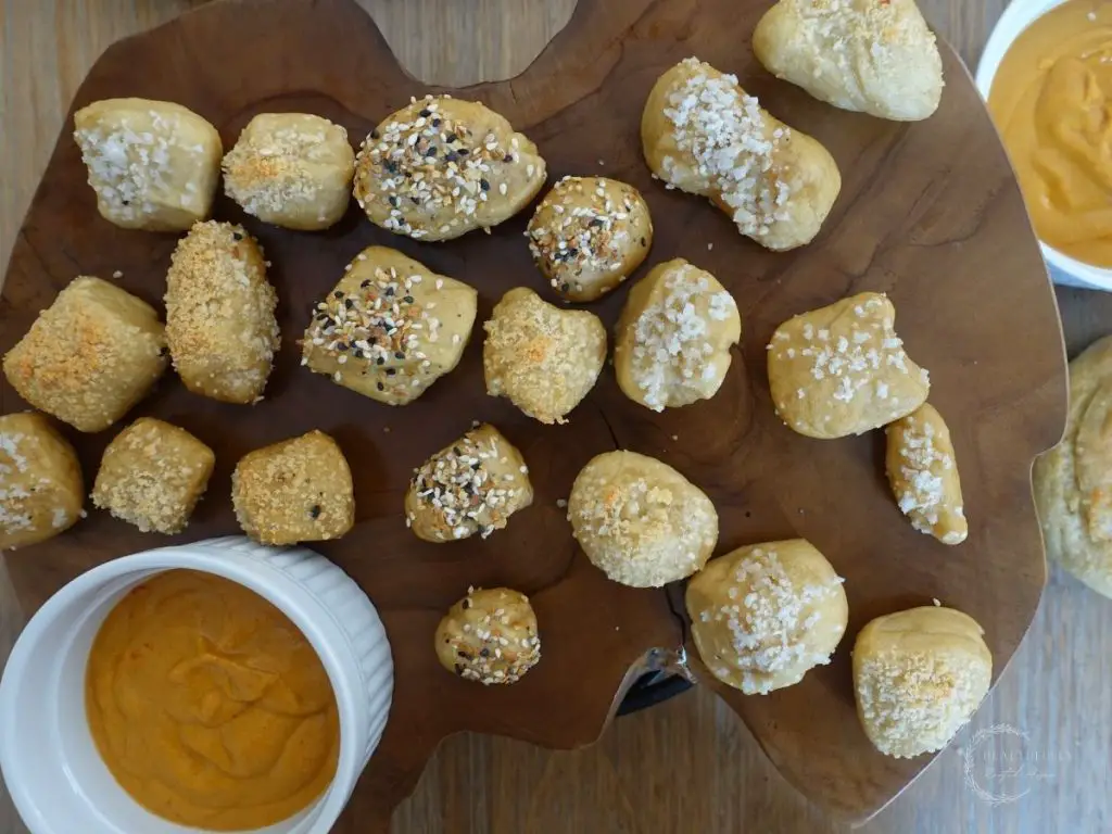 sourdough pretzel bites scattered on a wooden block with a couple bowls of cheese sauce next to them