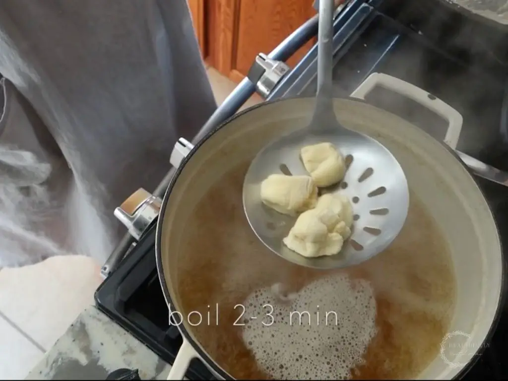 using a slotted spoon to submerge sourdough pretzel bite dough into a pot of boiling water