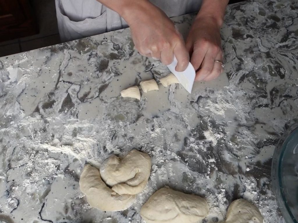 using a dough scraper to slice sourdough pretzel bites on a granite countertop