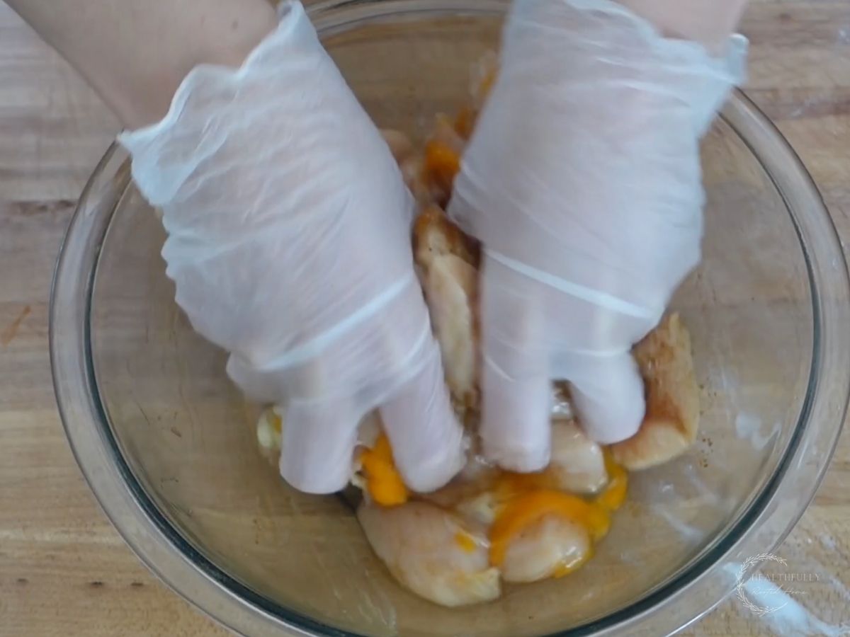 using gloved hands to combine the chicken breast chunks and marinade