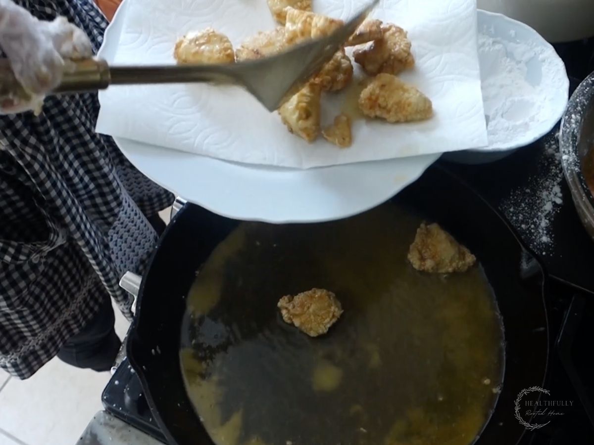 removing fried chicken from a cast iron skillet and adding to a paper towel lined plate