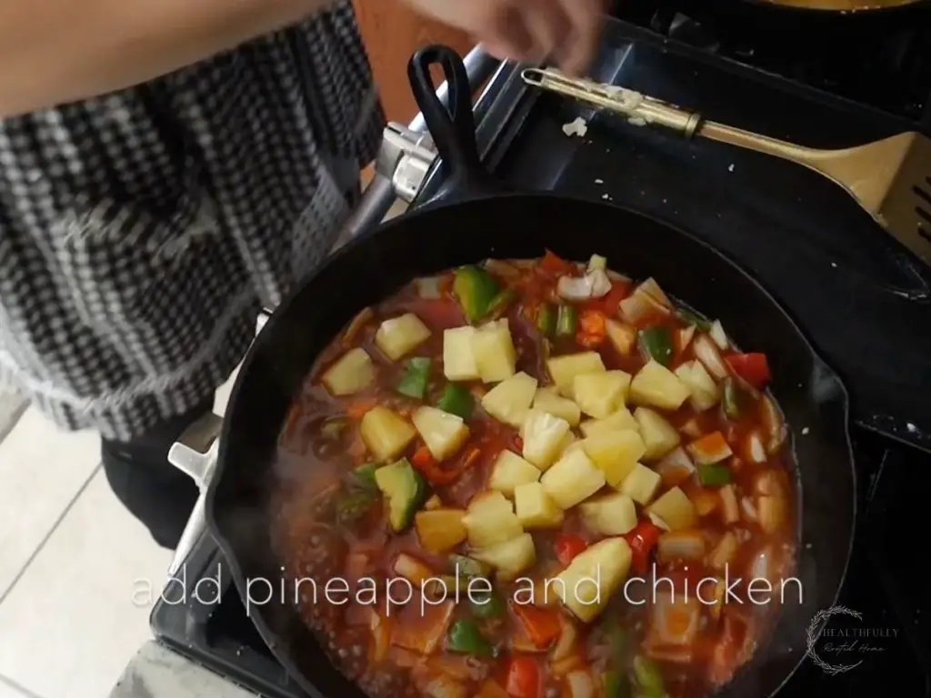 adding pineapple to the sweet and sour sauce vegetables in a cast iron skillet