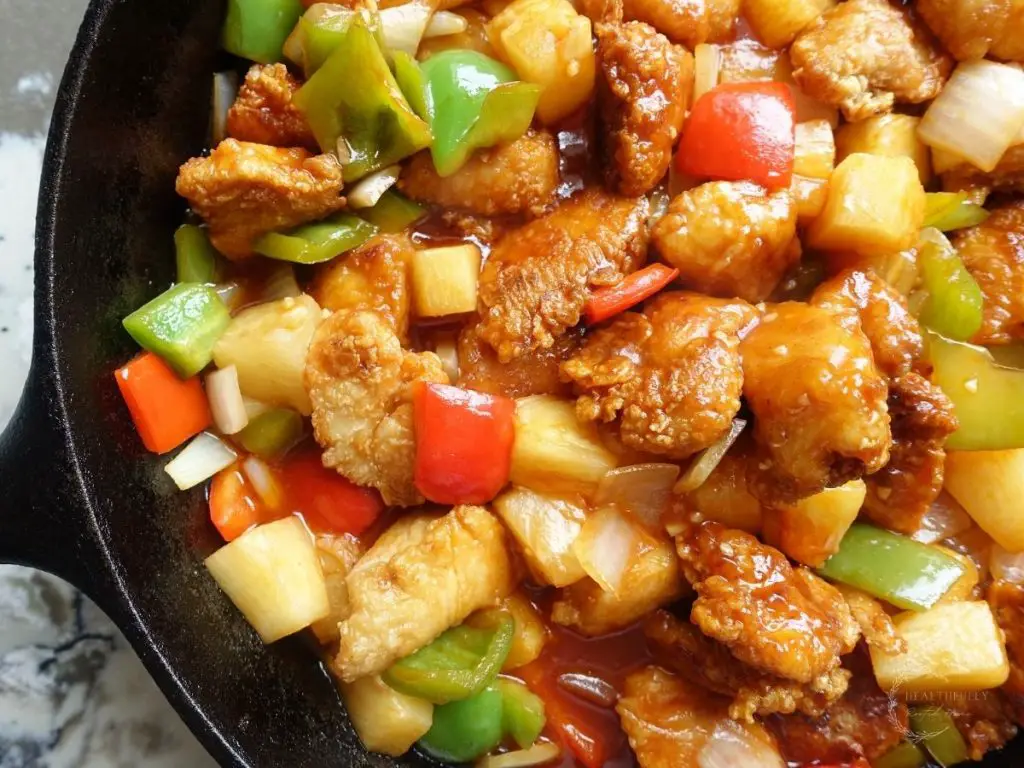 sweet and sour chicken hong kong style in a cast iron skillet with shiny bell peppers and pineapple
