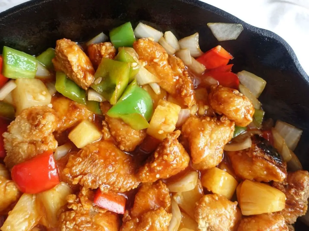 sweet and sour chicken hong kong style in a cast iron skillet close up with green bell peppers