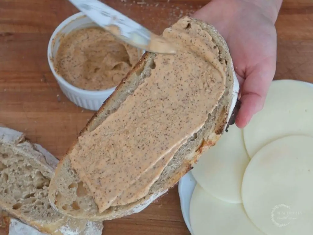 spreading ancho aioli over a slice of sourdough bread to make a grilled cheese sandwich