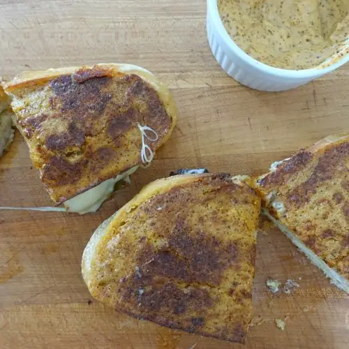 ancho aioli grilled cheese sandwiches made without butter laying flat on a wooden cutting board next to a bowl of ancho aioli