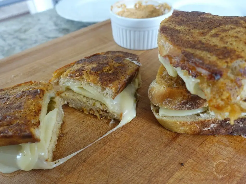 ancho aioli grilled cheese sandwich on a cutting board cut in half with cheese melting out of it