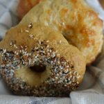 Sourdough discard bagels in a basket lined with a ticking striped tea towel showing off the bagel toppings of everything bagel seasoning and cheddar cheese