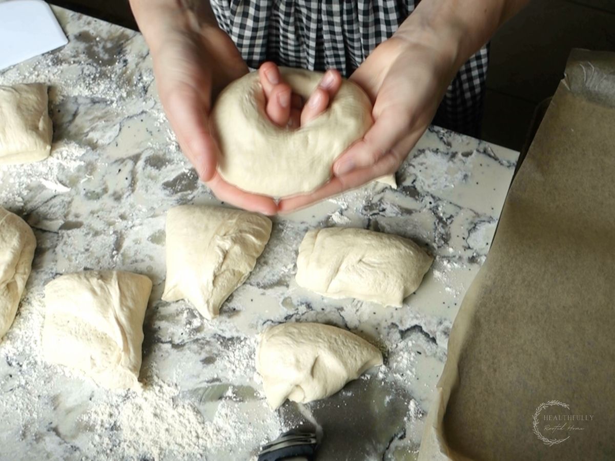 using hands to pull apart the middle of the bagel dough