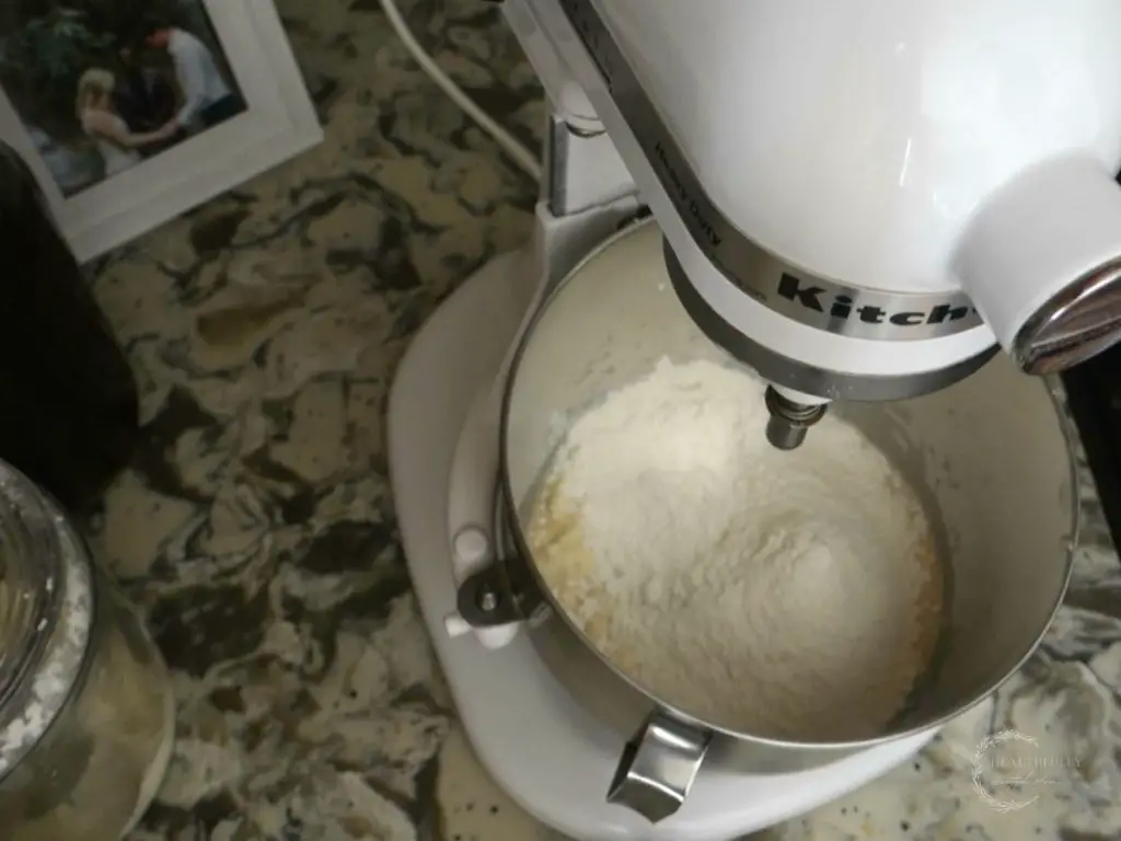 adding flour to a stand mixer to make sourdough discard bagel dough