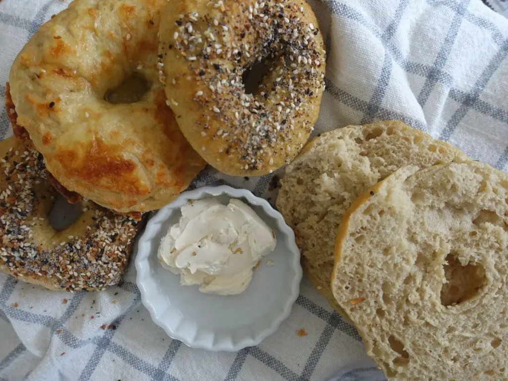 sourdough discard bagels lined up on top of eachother with one cut in half to show the crumb and a side of cream cheese next to them