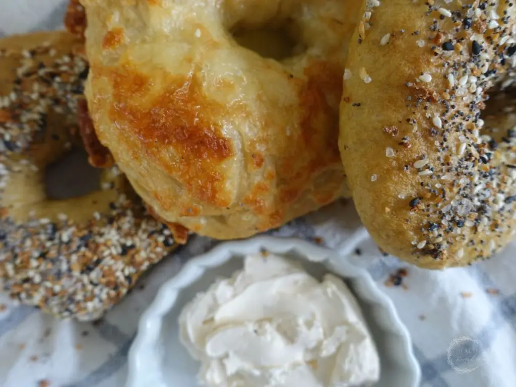 close up of sourdough discard bagels topped with cheddar cheese and everything bagel seasoning with a cup of cream cheese next to them