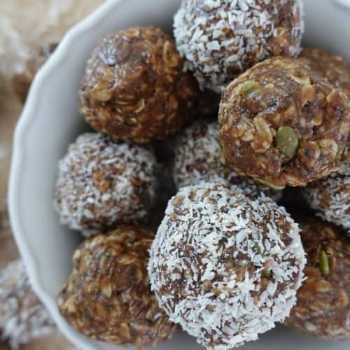 no bake boobie balls in a white bowl with half covered in coconut flakes and half not