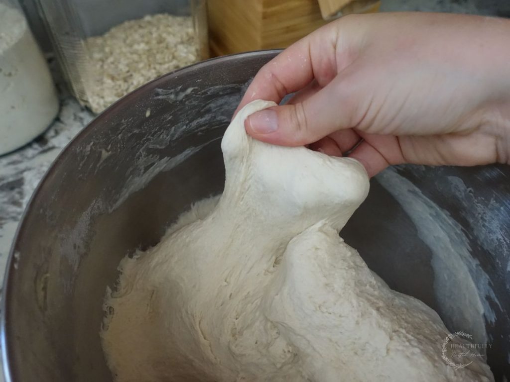 doing the windowpane test on a piece of fermented bread dough in the bowl of a stand mixer to see if it has been kneaded long enough