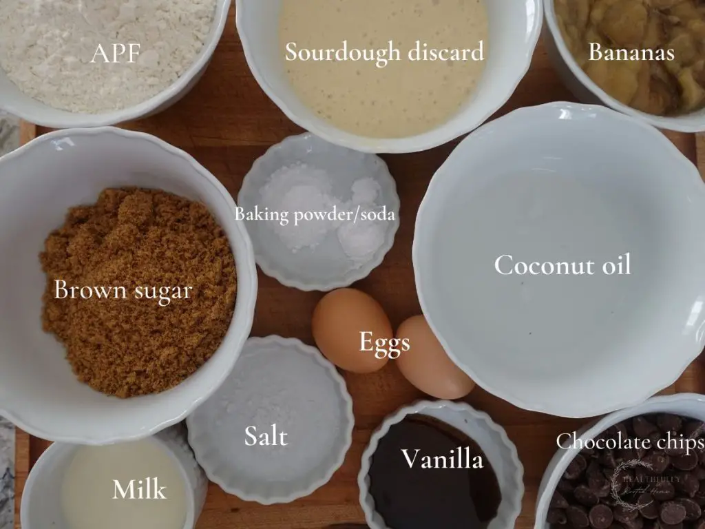 ingredients to make sourdough discard banana bread in white bowls with labels saying what each one is