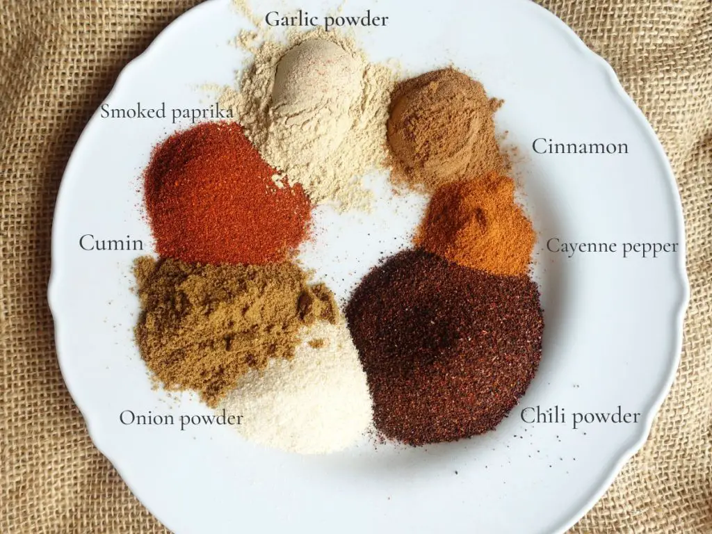 all the ingredients to make homemade low sodium taco seasoning on a white plate with labels saying what they are