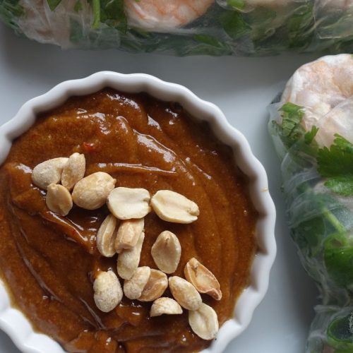 3 ingredient peanut sauce in a white bowl with crushed peanuts as garnish sitting next to homemade spring rolls