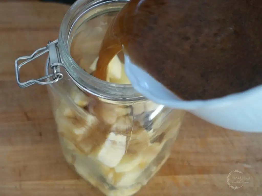 pouring liquid brine over diced apples in a fermentation jar