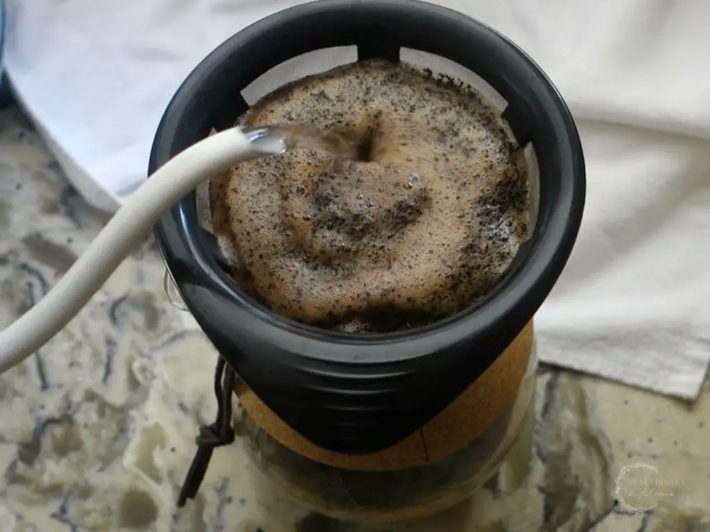 pouring water through a gooseneck kettle overtop coffee grounds in a hand drip coffee maker