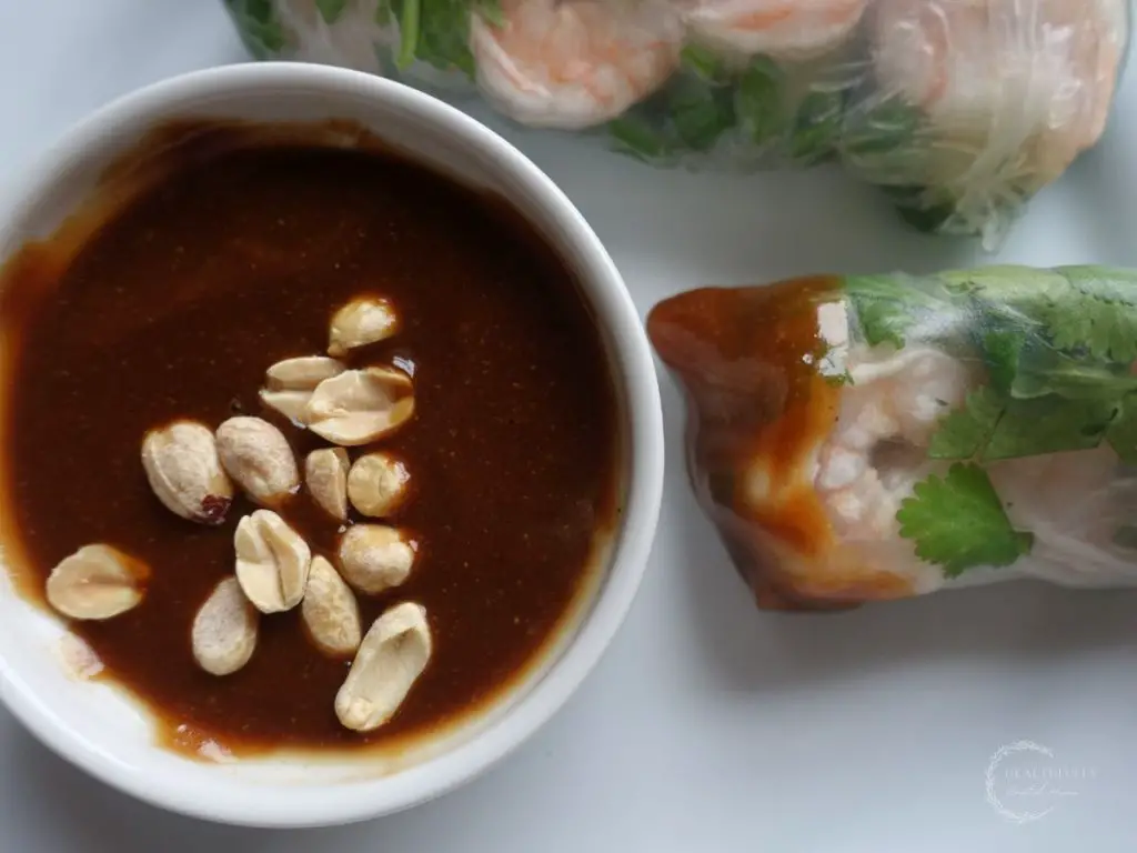 hoisin peanut sauce garnished with peanuts and a spring roll dipped in the sauce
