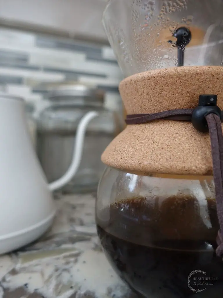 hand drip coffee in a chemex pour over carafe with a white electric gooseneck kettle in the background