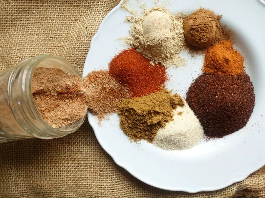 low sodium taco seasoning in a jar spilling out over a plate of spices - all of which are used to make the taco seasoning