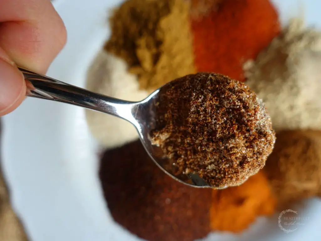 a spoon with low sodium taco seasoning on it above a plate with all the spices to make the recipe
