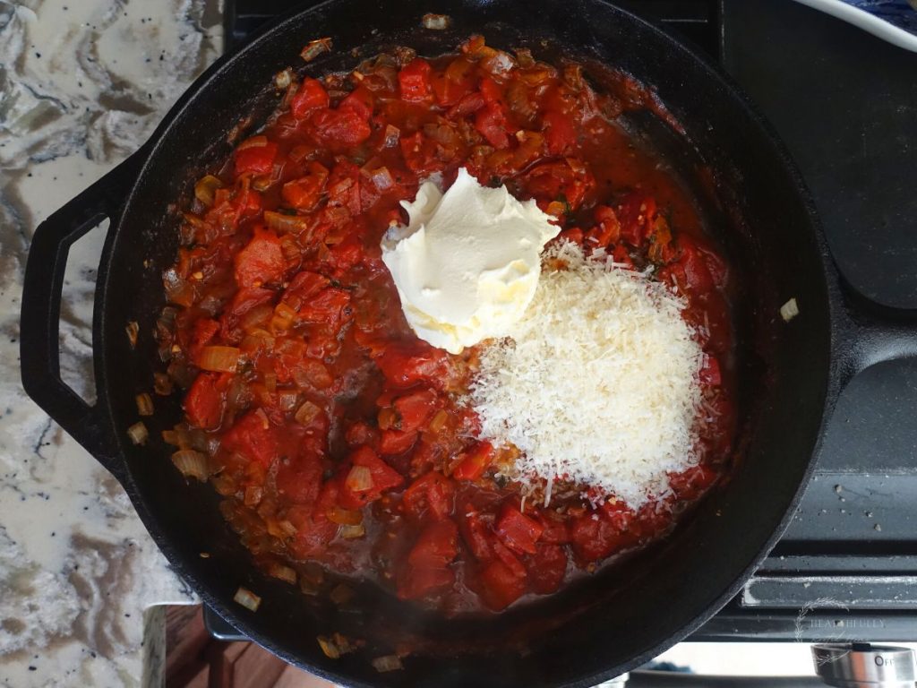 mascarpone and parmesan cheese overtop sauteed tomato sauce in a cast iron skillet