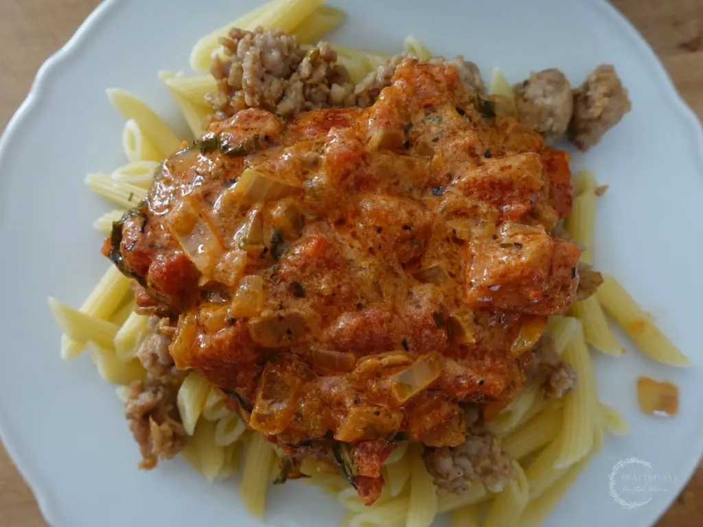 tomato mascarpone sauce served overtop a bed of pasta and italian sausage on a white plate