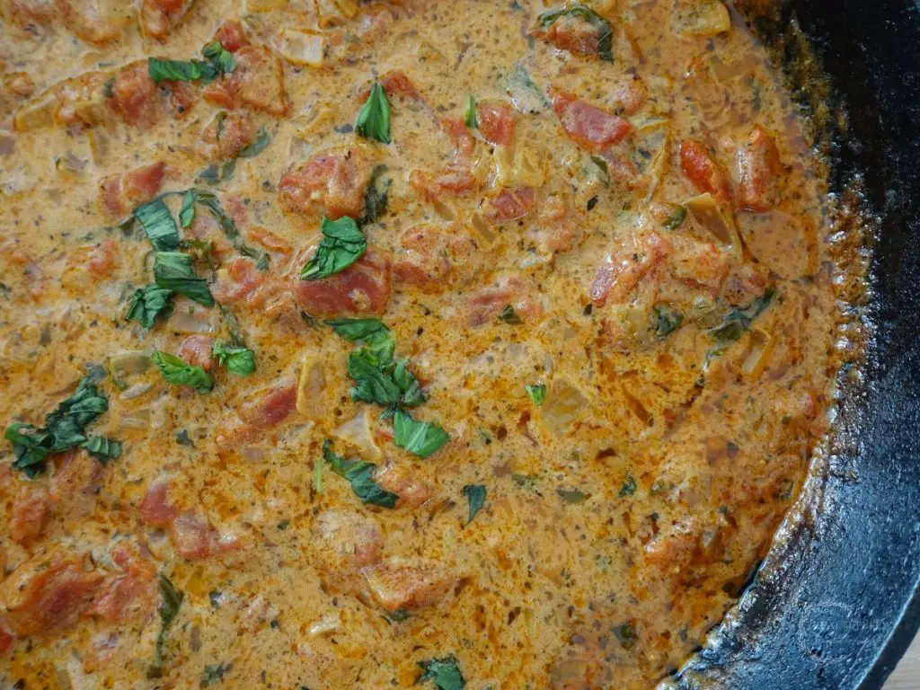 close up of tomato mascarpone sauce garniched with fresh basil in a cast iron skillet