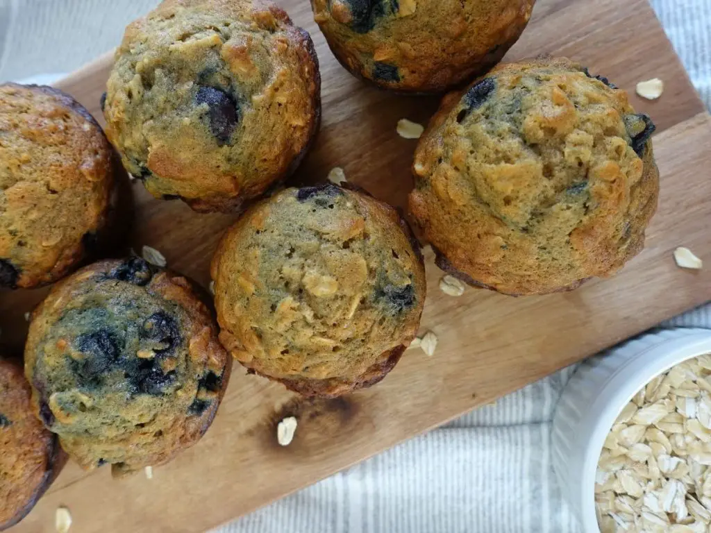close up of banana blueberry oatmeal muffins with oats surrounding them on a wooden platter