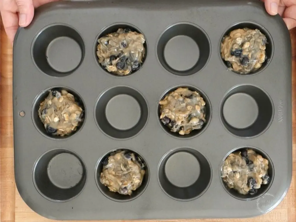 banana blueberry oatmeal muffin batter in a muffin tin with spaces between each muffin