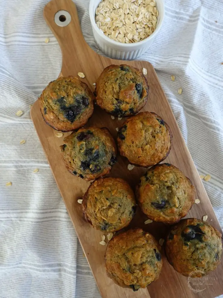 banana blueberry oatmeal muffins lined up on a serving board with a bowl of oats next to it