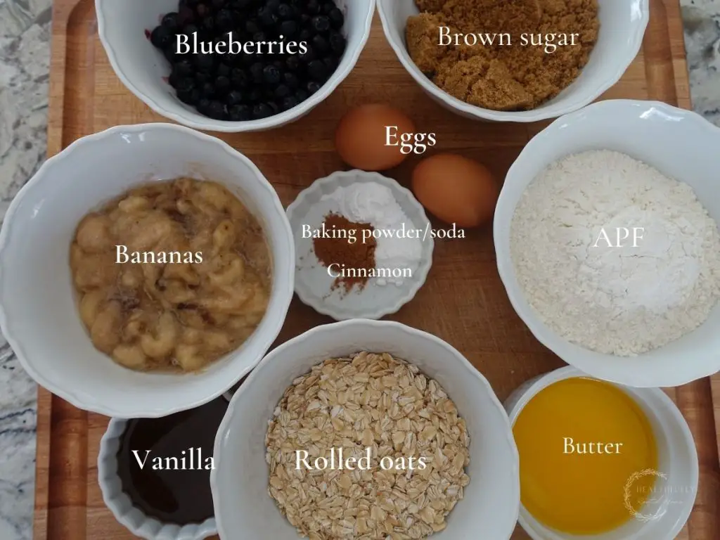 ingredients used to make banana blueberry oatmeal muffins in white bowls with labels saying what they are