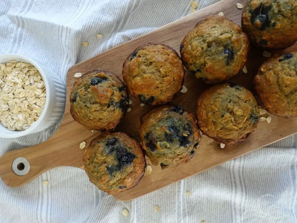 blueberry banana oatmeal muffins on a wooden serving platter with a cup of oats on the side