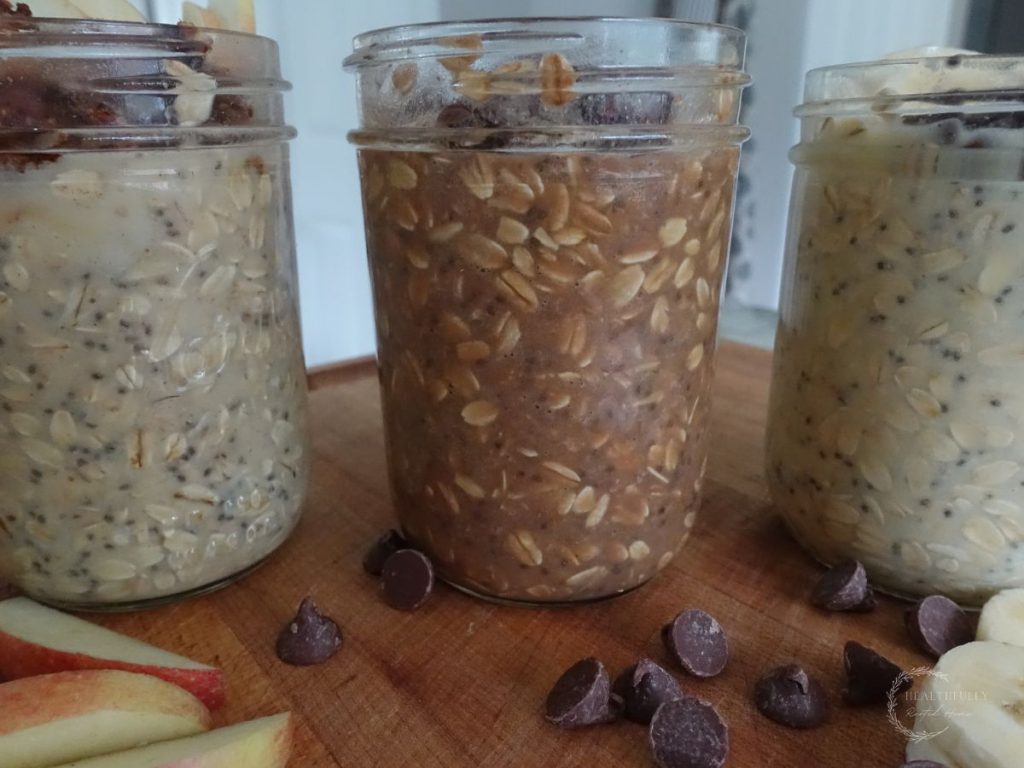 3 different types of high protein overnight oats in mason jars with chocolate chips apples and banana slices on the side