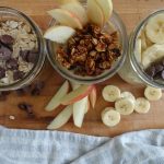 high protein overnight oats in 3 mason jars with 3 different flavors and toppings chocolate chips apples and bananas with a tea towel on the side for decor
