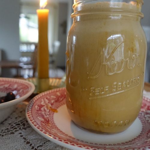 homemade salted caramel cold foam cold brew in a mason jar with a beeswax candle in the background on a festive red plate
